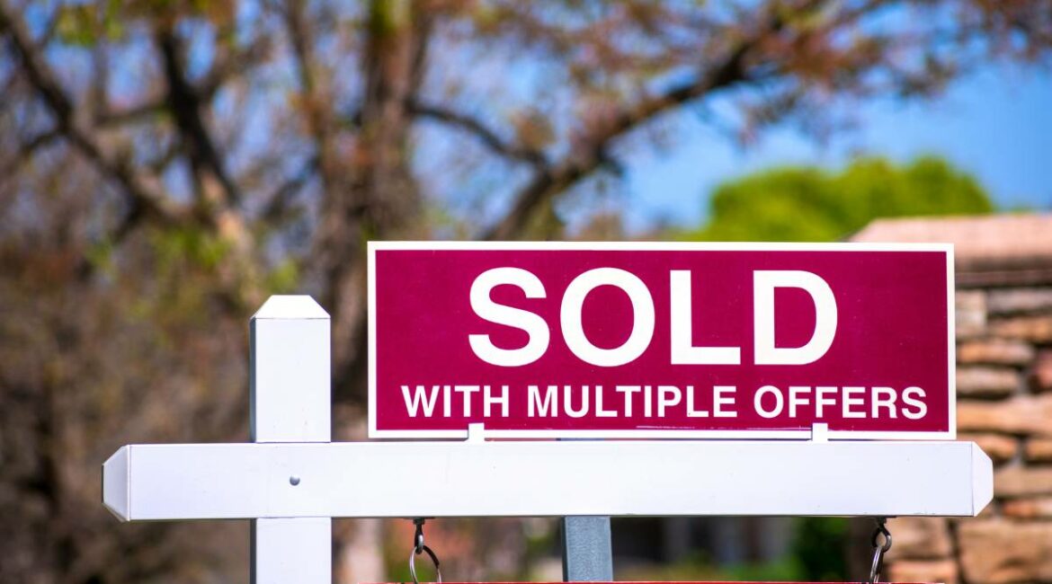 A sold sign with multiple offers written on it in front of a house