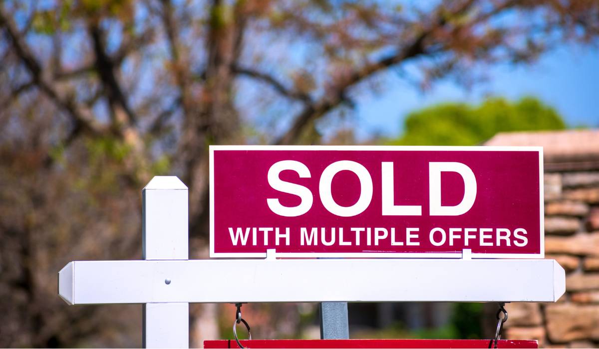 A sold sign with multiple offers written on it in front of a house
