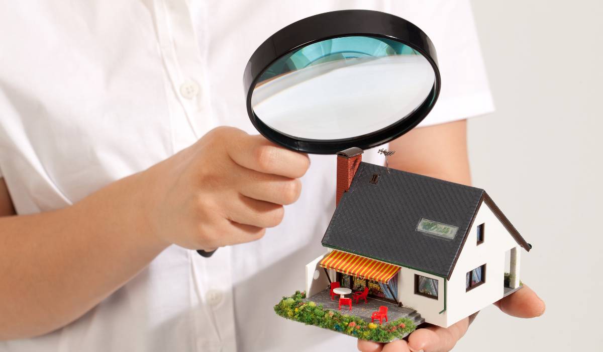 A person holding a magnifying glass over a miniature house