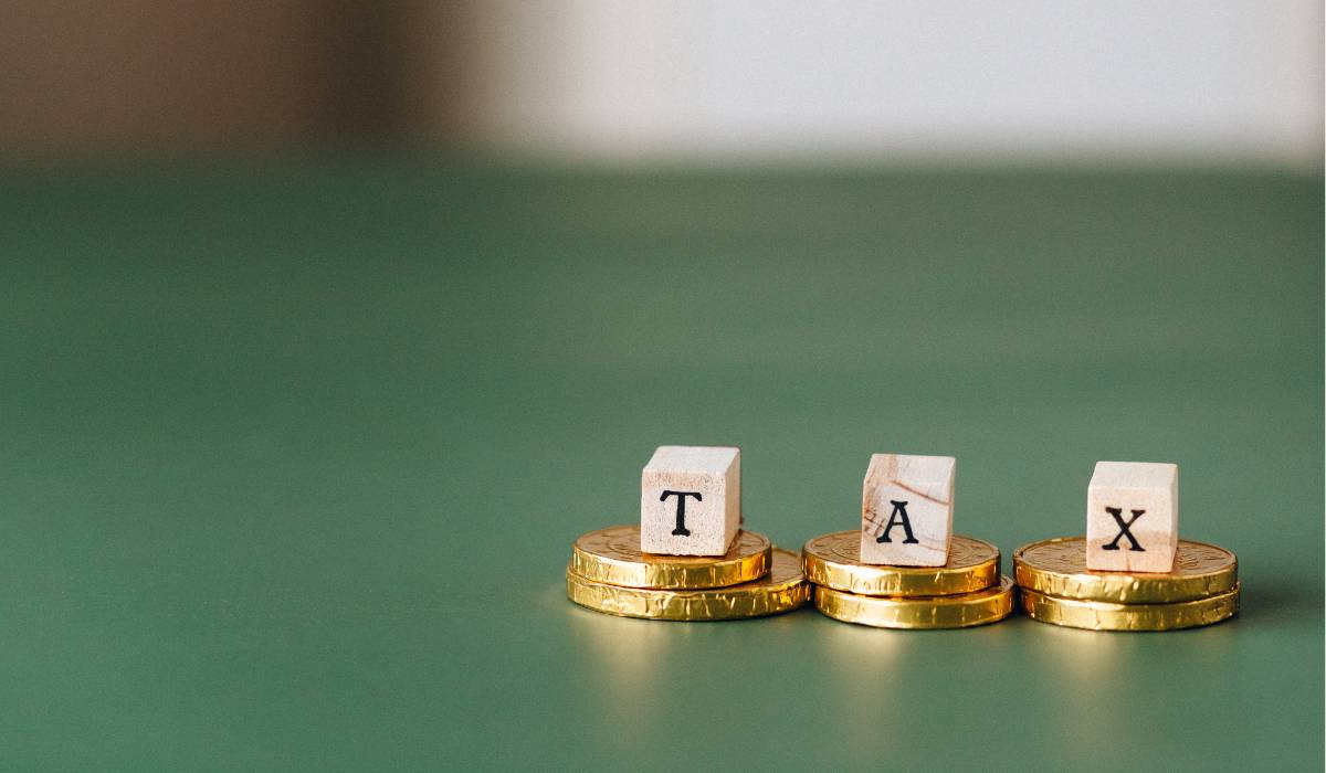 Golden coins spelling the word tax on top of stacks of coins on a green background to show land transfer tax