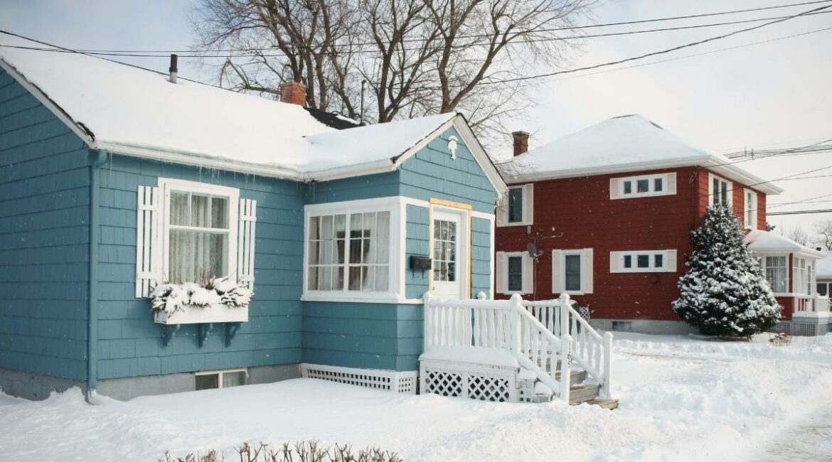 A cyan blue and a red house side by side covered in snow.