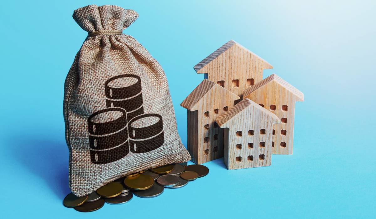 Wooden houses and a bag of coins on a blue background.
