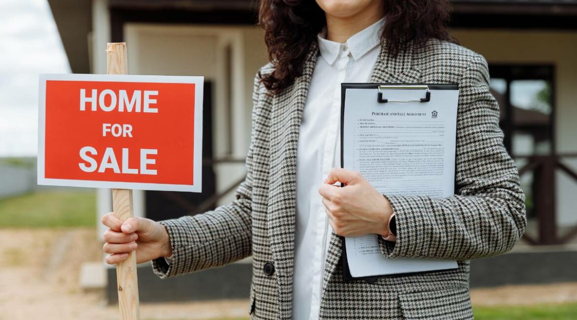 a realtor holding a home for sale sign in front of a house