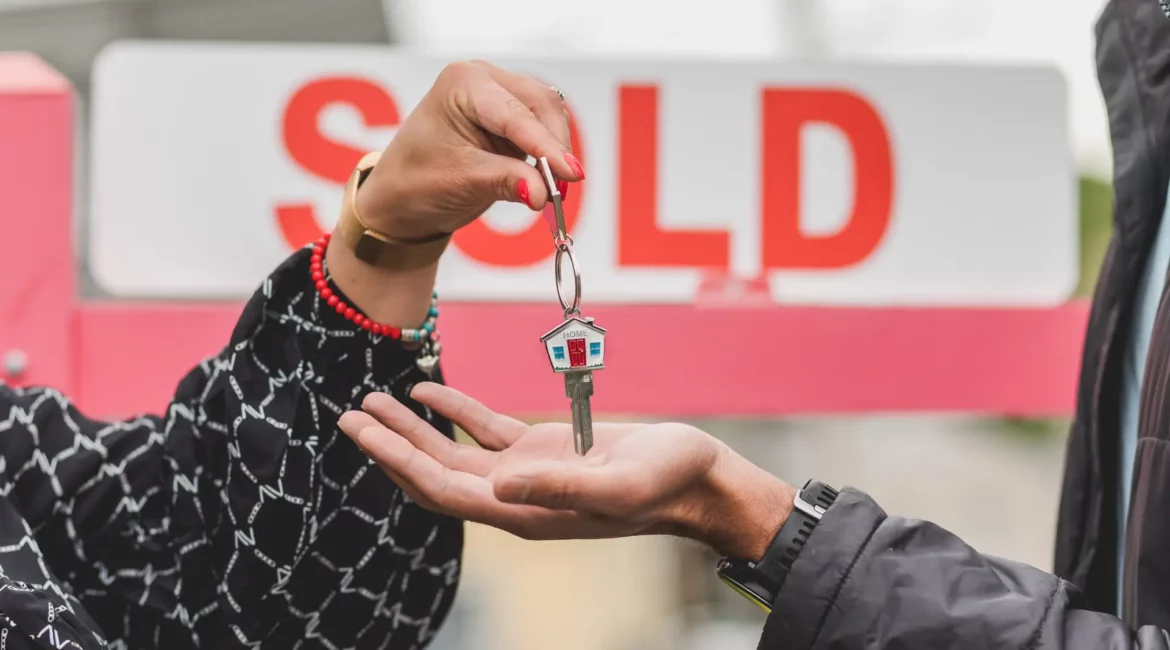 a person gives a key to another person with a sold sign on the background